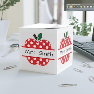 May include: White cube-shaped desk organizer with a red apple design. The apple has white polka dots and the text "Mrs. Smith" is written on a banner across the middle of the apple.