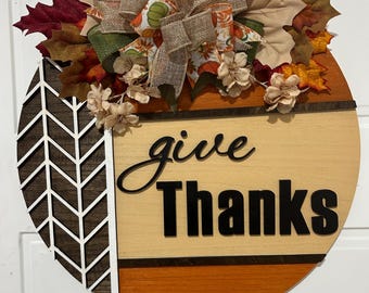 Okrągły wieszak na drzwi „Give Thanks” o średnicy 18 cali. Kolory: pomarańczowy, brązowy i kremowy.