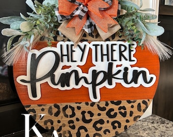 Okrągły jesienny wieszak na drzwi Hey There Pumpkin o średnicy 18 cali. Pomarańczowo-czarny wzór w panterkę.