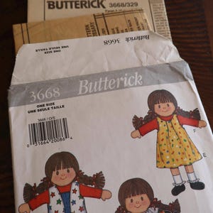 May include: A Butterick 3668 sewing pattern envelope for a doll, featuring illustrations of three dolls with brown hair in pigtails wearing different outfits, including a yellow dress, a star-print vest with blue overalls, and a floral dress with a ruffled collar.