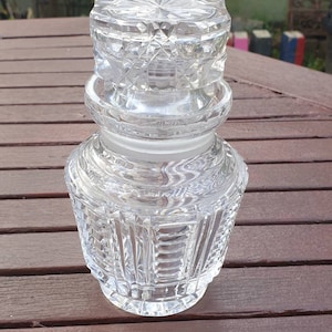 May include: A clear glass bottle with a decorative stopper. The bottle has a textured, diamond-shaped pattern.