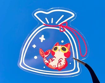 May include: A clear sticker featuring a cartoon cat-shrimp hybrid inside a blue bag with a red drawstring. The cat-shrimp has red and white markings and is wearing sunglasses. The sticker is held by black tweezers against a bright blue sky.