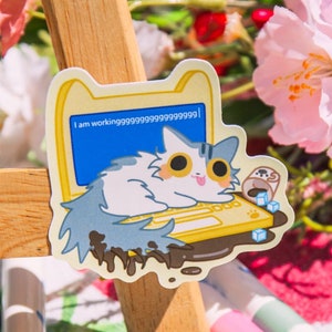 May include: Two stickers featuring a cartoon cat working on a laptop with the text "I am workinggggggggggggggggggggggggggg!" on the screen. The cat is sitting on a laptop that is covered in chocolate. The stickers are on a pink and green floral patterned surface.