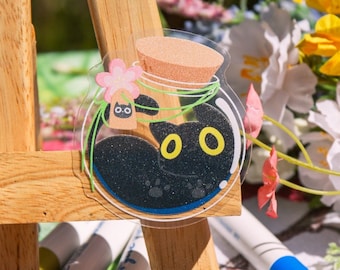 May include: Two black cat stickers in a clear jar with a cork top. The jar is decorated with a pink flower and green leaves. The stickers are on a white surface with a red apple design.
