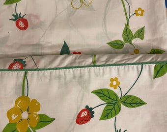May include: White fabric with a repeating pattern of strawberries, green leaves, and yellow and white flowers. The fabric has a green border. The design is a vintage style.