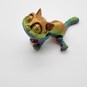 May include: A small, rainbow-colored, 3D printed cat figurine with large eyes and a playful expression.