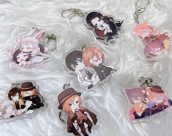 Puede incluir: Un conjunto de ocho llaveros de personajes de anime con varios personajes de la serie de anime "Bungou Stray Dogs". Los llaveros están hechos de acrílico transparente y presentan ilustraciones coloridas de los personajes.