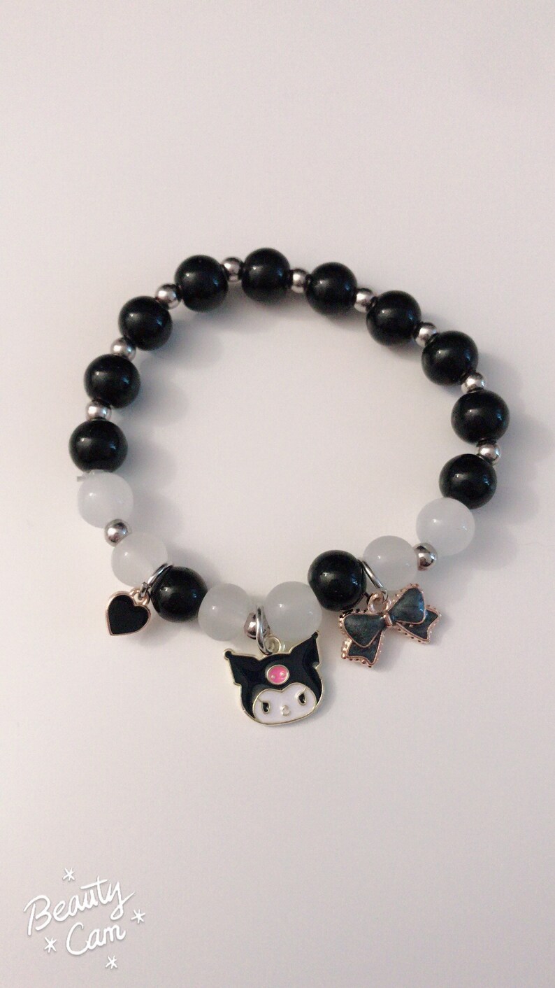 Op de afbeelding: Zwart-witte kralen armband met een zwart hart, een zwart-witte strik en een zwart-witte figuur bedel.