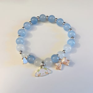 Op de afbeelding: Een lichtblauwe en witte kralen armband met een bedel van een cartoon hond en twee strikken.