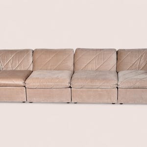 May include: A modular sofa composed of four connected sections upholstered in a light beige velvet fabric. The backrests and seat cushions feature a distinct diagonal quilted pattern, creating a textured surface across the entire piece.