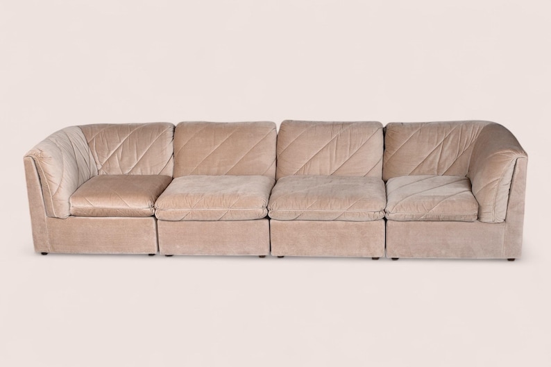 May include: A modular sofa composed of four connected sections upholstered in a light beige velvet fabric. The backrests and seat cushions feature a distinct diagonal quilted pattern, creating a textured surface across the entire piece.