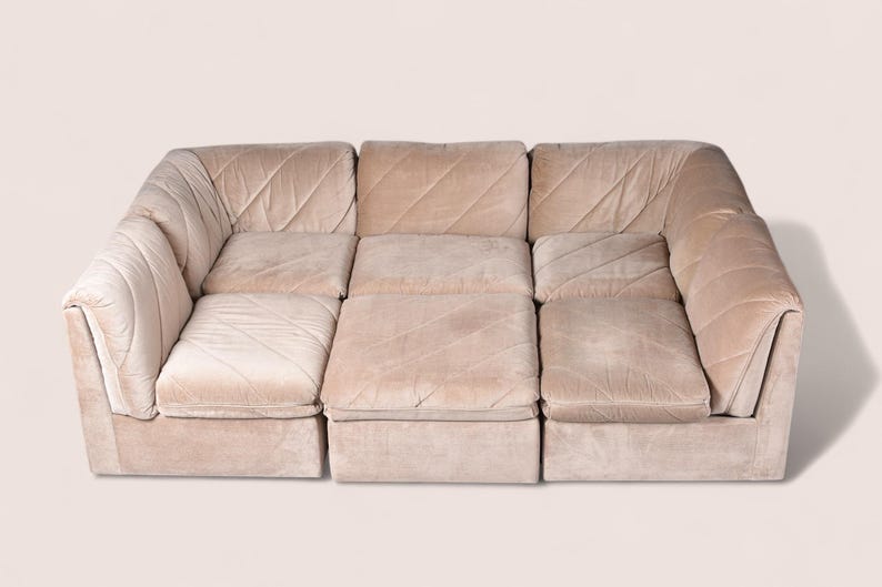 May include: A modular sectional sofa upholstered in a light beige velvet fabric. The sofa features a low-profile design with three distinct seating sections, each displaying a subtle diagonal quilted pattern across the cushions and backrests.