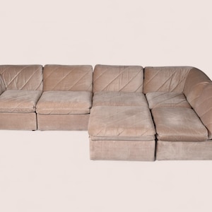 May include: A modular sectional sofa upholstered in a light beige fabric with a diagonal quilted pattern. The sofa consists of multiple connected seating units, including a corner piece and an extended chaise section, featuring low backrests.