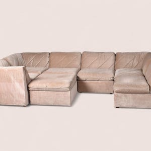 May include: A modular sectional sofa upholstered in a light beige fabric. The sofa features multiple connected seating sections with low backrests and a distinct diagonal stitched pattern across the cushions, creating a unified seating arrangement.