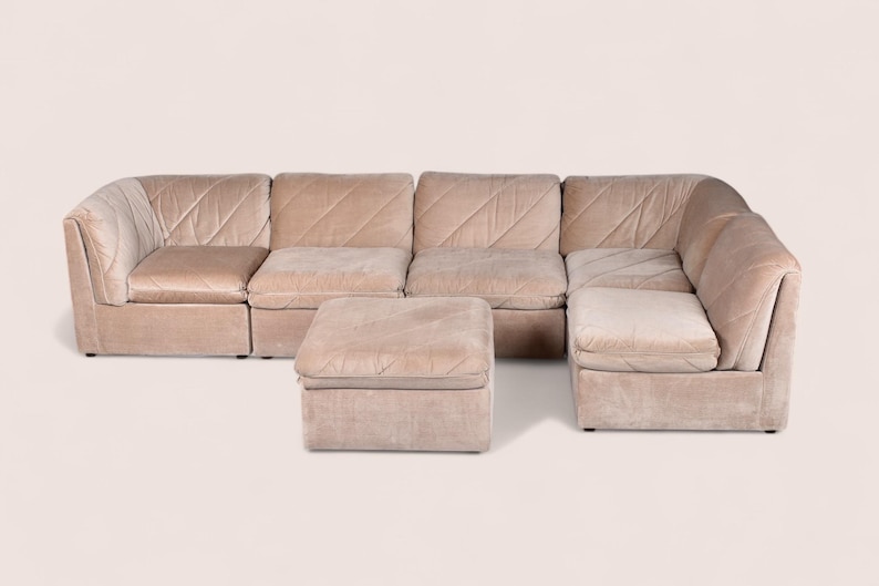May include: A modular sectional sofa in a light beige velvet fabric featuring a diagonal quilted pattern across the backrests and seat cushions. The set includes multiple connected seating units arranged in an L-shape with a matching square ottoman.
