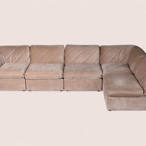 May include: A modular sectional sofa upholstered in a light beige fabric with a subtle diagonal quilted pattern. The sofa features a low-profile design with four distinct seating sections and a corner unit, creating an L-shaped configuration.