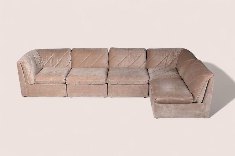May include: A modular sectional sofa upholstered in a light beige fabric with a subtle diagonal quilted pattern. The sofa features a low-profile design with four distinct seating sections and a corner unit, creating an L-shaped configuration.