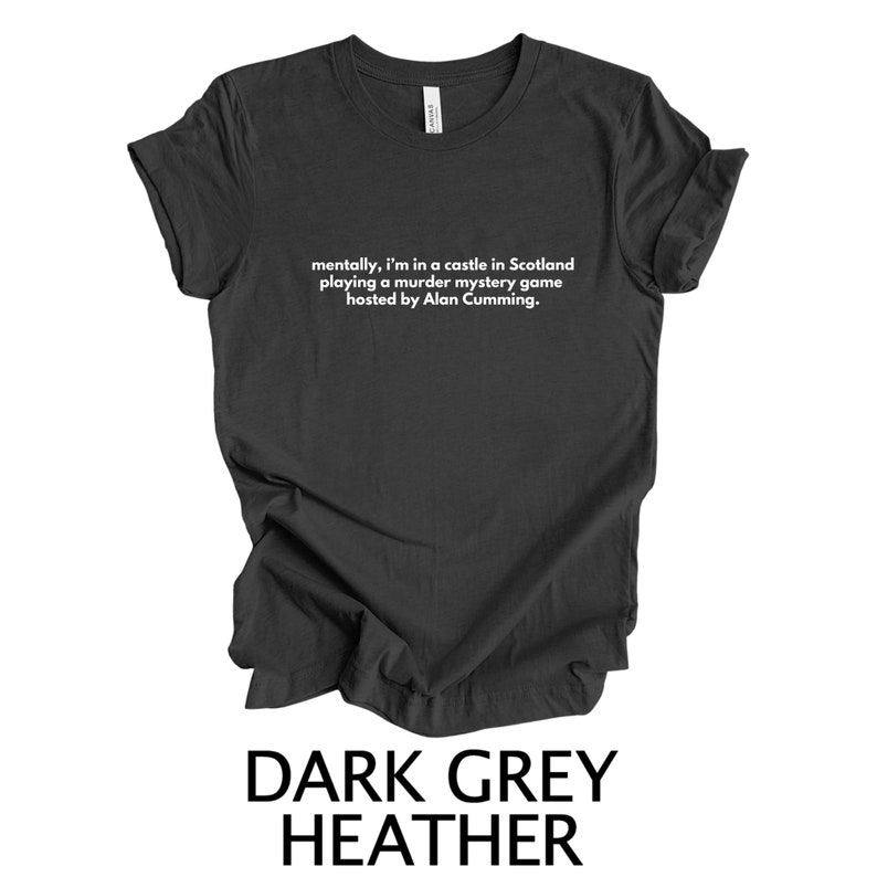 May include: Dark grey heather t-shirt with white text that reads "mentally, I'm in a castle in Scotland playing a murder mystery game hosted by Alan Cumming."
