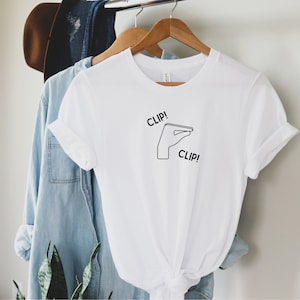 May include: White t-shirt with a black line drawing of a hand making a clipping motion. The text "CLIP!" appears twice on the shirt.