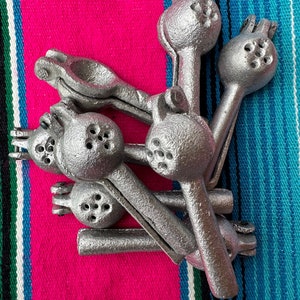 May include: Five silver lime squeezers, also known as a citrus press, are stacked on top of each other. The squeezers are made of metal and have a textured surface. They are on a pink and blue striped fabric.