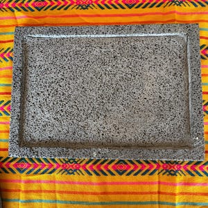 May include: A gray rectangular stone serving tray with a rough, textured surface. The tray is made of volcanic rock and has a natural, rustic look.