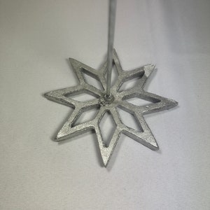 May include: A silver-colored rosette iron with an eight-pointed star design. The iron has a long, thin handle extending from the center of the star. The star's points are sharp and the design is open.