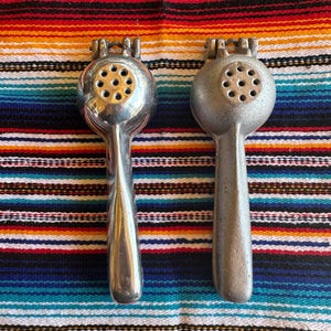 May include: Two silver citrus juicers with a gold-colored top and a handle. The juicers are on a colorful striped fabric.