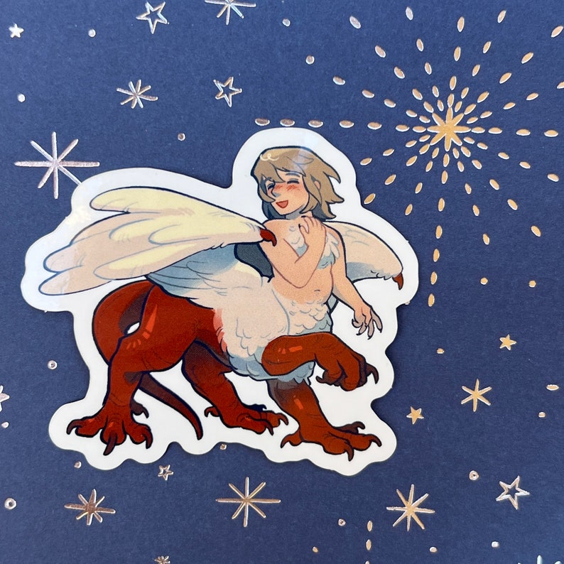 May include: A sticker featuring a cartoon illustration of a white and red winged creature with a human-like head and body. The creature has a white and brown feathered body and a red tail. The creature is smiling and has a white wing on its back. The sticker is on a blue background with white stars.