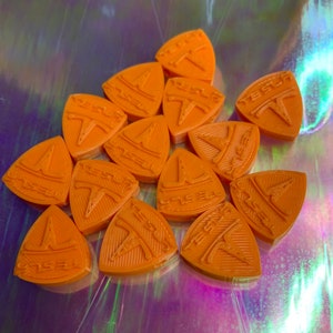 May include: A group of 13 orange plastic triangular guitar picks with the Tesla logo embossed on each pick.