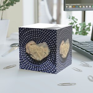 May include: A blue and white notepad with a heart-shaped rock on the front. The rock is a light brown color and has a rough texture. The notepad has a white top and a blue base with white polka dots.