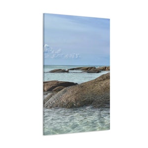 May include: A scenic view of a rocky beach with clear blue water and a few seagulls perched on the rocks. The sky is a light blue with a few white clouds.