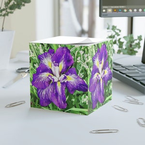 May include: A cube-shaped notepad with a purple and white iris flower design on a green background. The notepad is perfect for jotting down notes, ideas, or reminders.