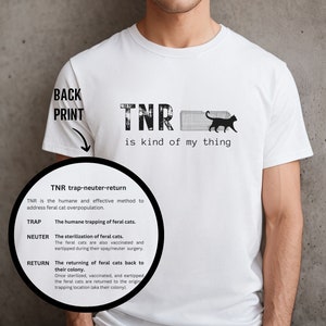 May include: White t-shirt with a black graphic that says "TNR is kind of my thing". The graphic also includes a black cat in a cage. The text "TNR trap-neuter-return" is written below the graphic, along with an explanation of what TNR is.