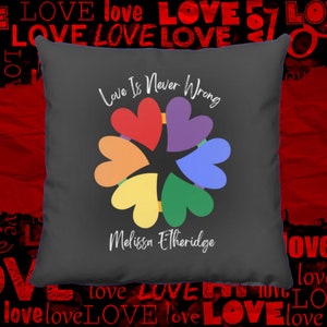 Peut inclure: Un coussin gris avec le texte "Love Is Never Wrong" en écriture cursive blanche. Un motif de cœur arc-en-ciel est centré sur l'oreiller, avec le texte "Melissa Etheridge" en dessous du motif.