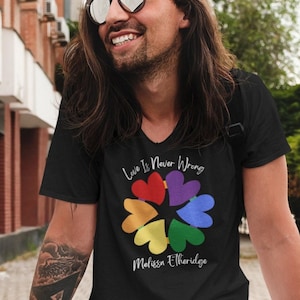 May include: A black V-neck t-shirt with the text "Love Is Never Wrong" and a rainbow heart design. The name "Melissa Etheridge" is printed below the design.