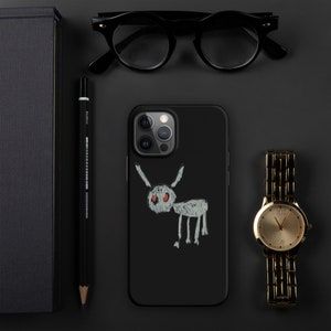 Puede incluir: Funda negra para iPhone con una ilustración dibujada a mano de una criatura con ojos rojos. También se ven un reloj de pulsera dorado, gafas negras, un lápiz negro y un cuaderno negro.