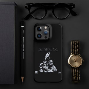 Puede incluir: Funda negra para iPhone con el texto "For All The Dogs" y un gráfico de una persona y perros. También se ven un reloj dorado, gafas negras y un lápiz.