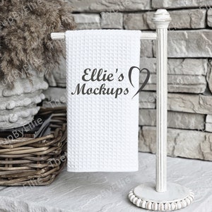 May include: White kitchen towel hanging on a white metal towel rack. The towel has the text "Ellie's Mockups" with a heart design.