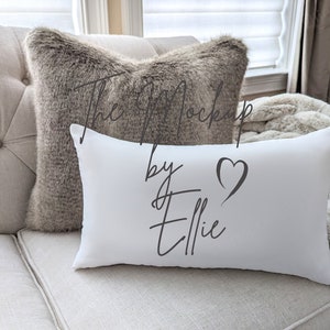 Puede incluir: Almohada rectangular blanca con el texto "The Mockup by Ellie" y un símbolo de corazón en gris.