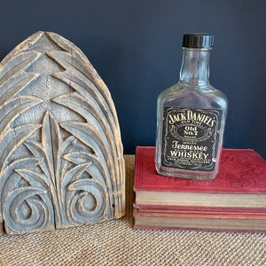 Puede incluir: Una botella de vidrio transparente de whisky de Tennessee Jack Daniel's, marca Old No. 7, sobre una pila de libros rojos. La botella tiene una tapa negra y una etiqueta negra con letras doradas.