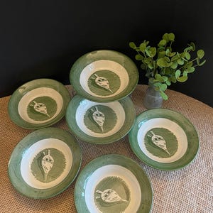 Może przedstawiać: Zestaw sześciu zielonych i białych ceramicznych misek z motywem rzodkiewki. Miski są wszystkie tego samego rozmiaru i kształtu i mają rustykalny, wiejski charakter.