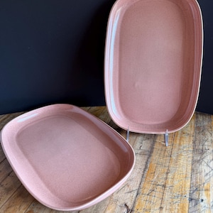 Könnte beinhalten: Zwei ovale Servierplatten in Rosa mit einer gesprenkelten Oberfläche. Die Platten sind aus Keramik und haben einen leicht erhöhten Rand.