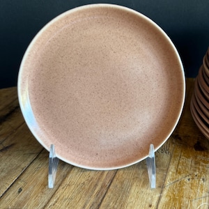 Könnte beinhalten: Ein hellrosa Teller aus Keramik mit einer gesprenkelten Textur. Der Teller liegt auf einer Holzoberfläche.