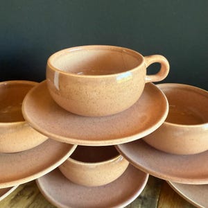 Könnte beinhalten: Ein Set aus sechs rosafarbenen Keramik-Teetassen und Untertassen. Die Tassen und Untertassen haben eine gesprenkelte Textur.