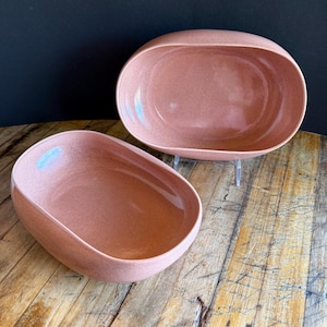 Könnte beinhalten: Zwei ovale Servierschalen aus hellrosa gesprenkelter Keramik. Die Schalen stehen auf einer Holzoberfläche.