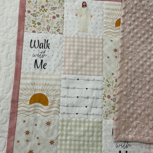 May include: A patchwork quilt with a pink border and backing. The quilt features squares with floral, gingham, and star patterns. The words "Walk with Me" are printed on the quilt, along with an image of Jesus and a sun.