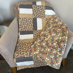 May include: A brown and gray patchwork quilt with a fleece blanket featuring a monkey pattern on top. The quilt has a white, gray, and brown checkered pattern.
