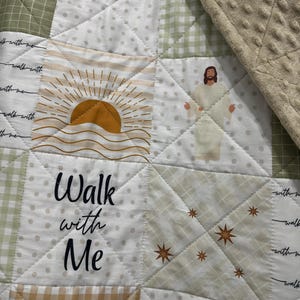 May include: A patchwork quilt featuring squares of various patterns and colors, including white with polka dots, green gingham, and tan stripes. The quilt has the words "Walk with Me" and images of a sunrise, stars, and a figure in white robes.