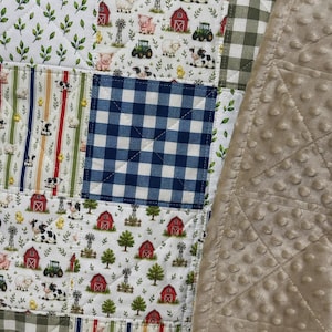 May include: A patchwork quilt featuring squares with farm-themed prints of red barns, green tractors, cows, pigs, sheep, and chicks, alternating with blue and white gingham, green leaf patterns, and a solid beige minky fabric with a dimpled texture.