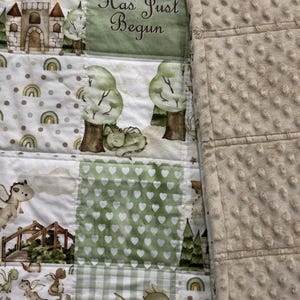 May include: A patchwork baby blanket featuring a whimsical dragon theme. The quilt showcases various patterns, including dragons, castles, trees, and hearts in shades of green, brown, and white. The text "My Reign Has Just Begun" is also visible.